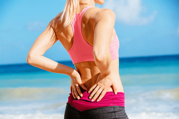 woman in workout clothes on beach holding lower back