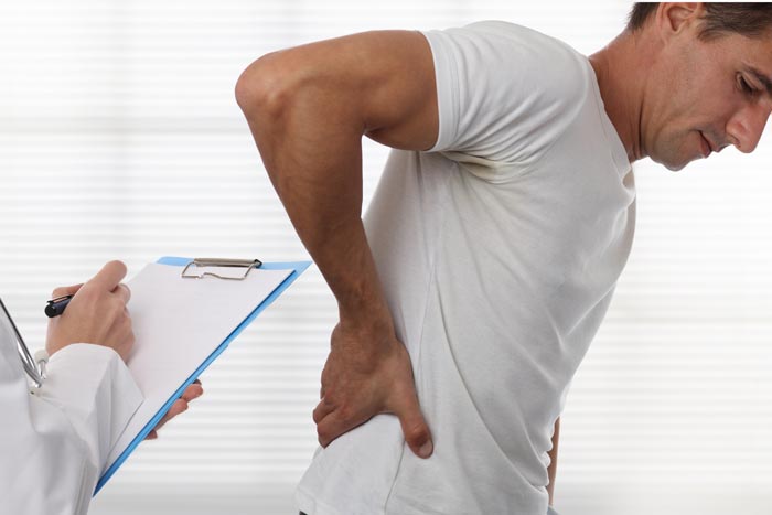 patient holding lower back while doctor examines him